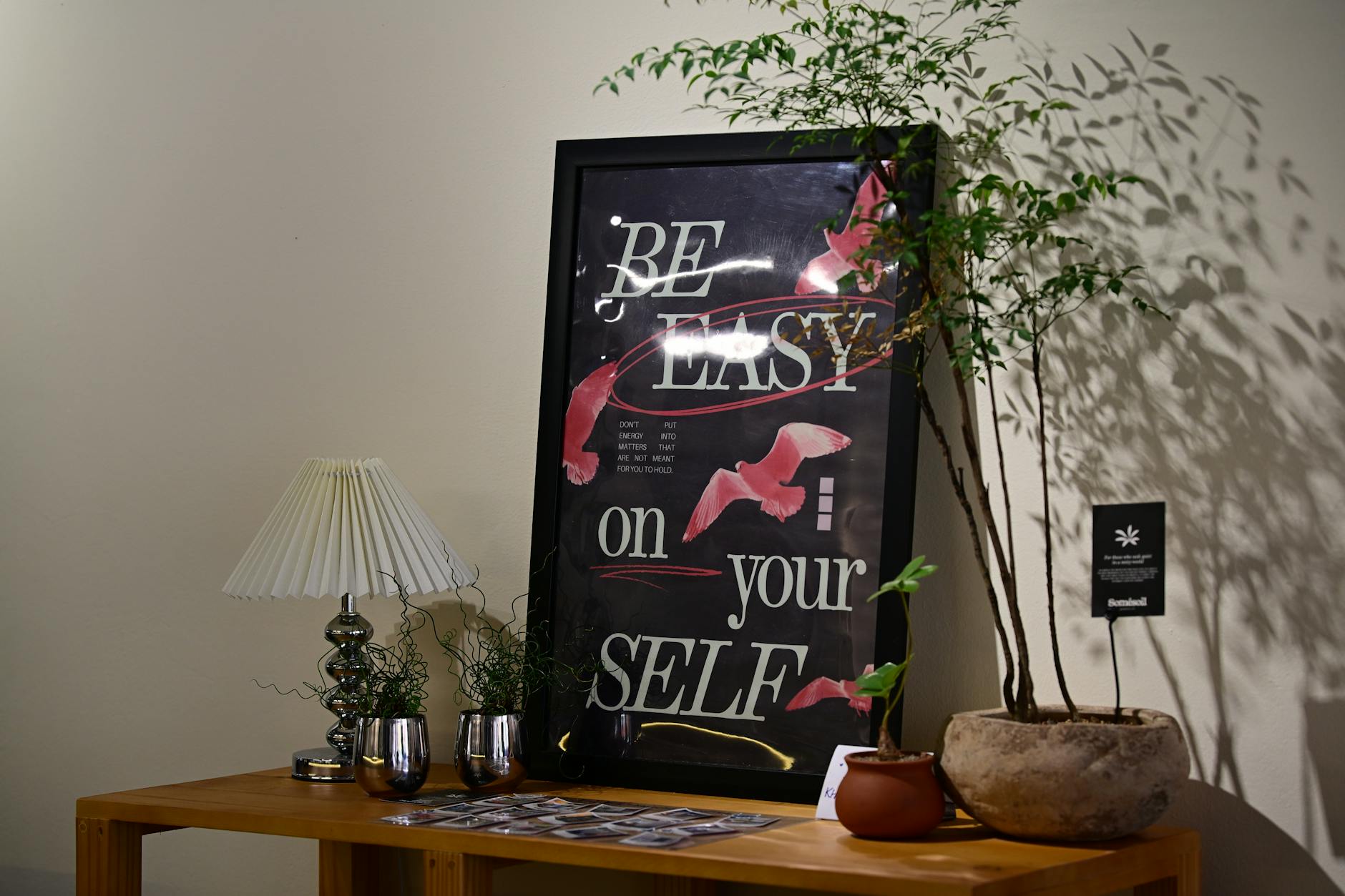 Stylish wall art with motivational text alongside a table with plants and lamp.