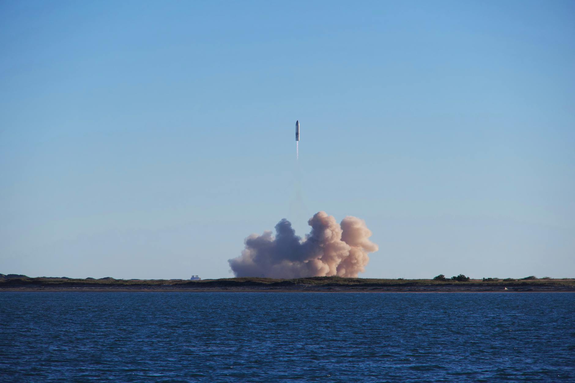 A rocket launch with smoke trails over South Padre Island, viewed across the ocean.