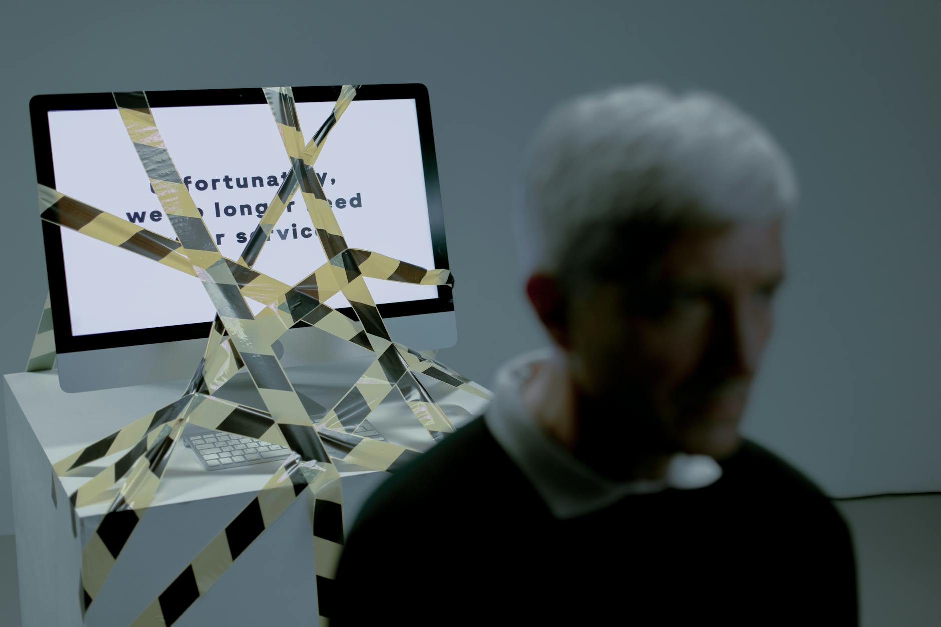 A senior man facing the reality of unemployment highlighted by a computer screen and warning tape.